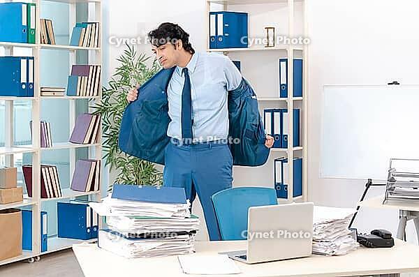 Young handsome male employee with too much work in the office [IBR125118018]