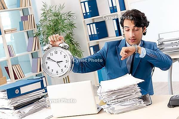Young handsome male employee with too much work in the office [IBR125118021]