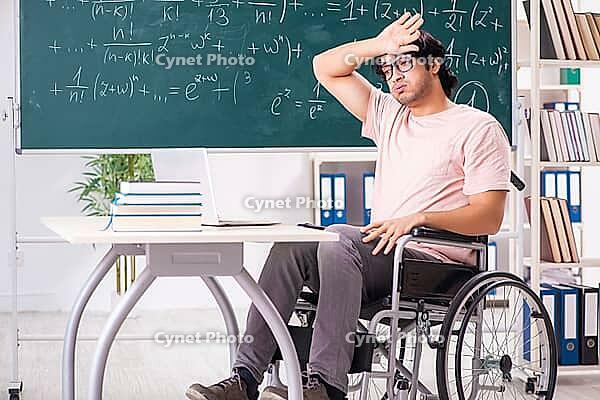 Young handsome man in wheelchair in front of chalkboard [IBR125118036]