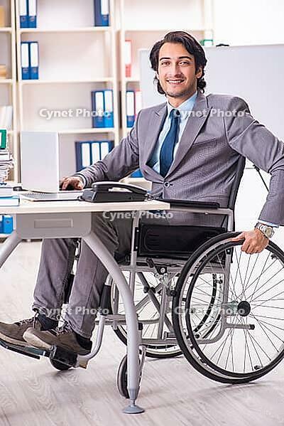 Young handsome employee in wheelchair at the office [IBR125118048]