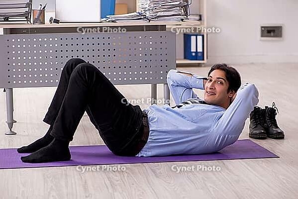 Young handsome male employee doing exercises in the office [IBR125141720]