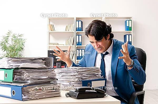 Young handsome busy employee sitting in office [IBR125141731]