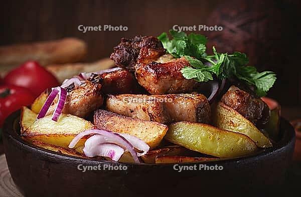 Ojakhuri, fried meat with potatoes, in ketsi, on a wooden table, Georgian cuisine, against a background of fresh ingredients [IBR125163378]