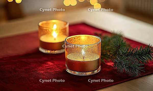 Two glass candle holders with golden candles, placed on a red velvet table runner with a small pine branch nearby. AI generated [IBR125167396]