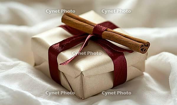 Small, wrapped present with a red ribbon and a cinnamon stick on top, placed on a white background. AI generated [IBR125167412]