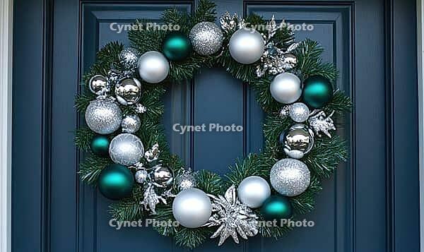 Simple white wreath with silver and green ornaments, hanging on a dark blue door, illuminated by natural daylight. AI generated [IBR125167426]