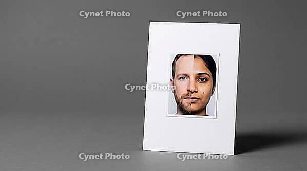 Passport-format identity photograph card showing morphed composite face, two different faces joined at vertical centerline, face morphing identity fraud concept, grey background, studio shot, AI generated [IBR125167455]