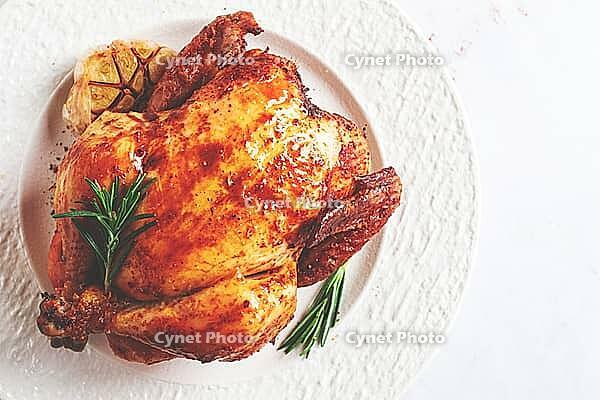 Baked chicken on a white platter with herbs and garlic, on a light background, homemade, no people [IBR125177932]