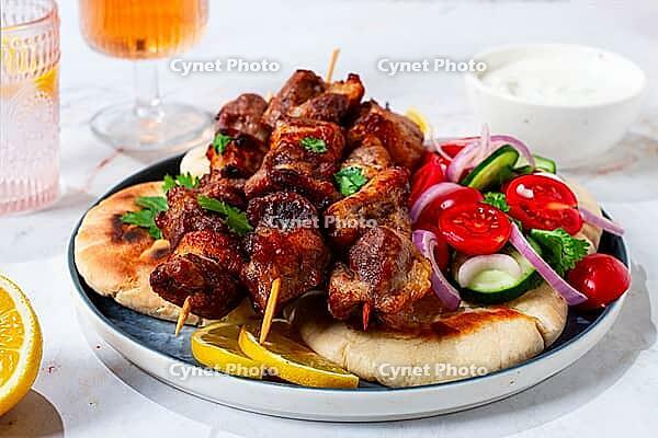 Souvlaki, a Greek dish, grilled meat shish kebab, on a plate with flatbreads, and lemon slices, grilled meat shish kebab, served with lavash, salad and drinks where there are no people [IBR125177933]