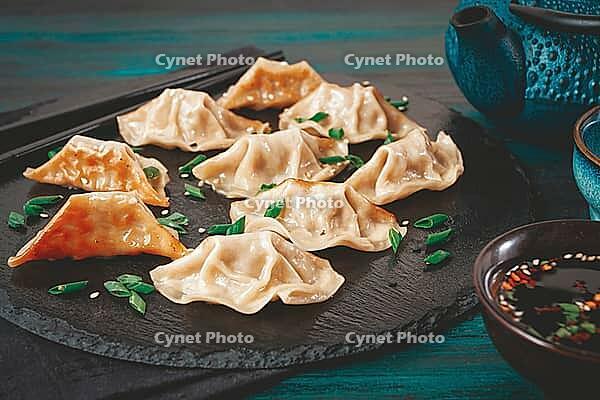 Gyoza, on a black stone platter, with a tetsubin teapot, a bowl with soy sauce, on a wooden table, dark style, no people [IBR125178017]