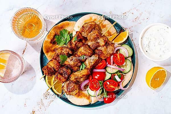 Souvlaki, a Greek dish, grilled meat shish kebab, on a plate with flatbreads, and lemon slices, grilled meat shish kebab, served with lavash, salad and drinks where there are no people [IBR125178018]