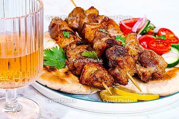Souvlaki, a Greek dish, grilled meat shish kebab, on a plate with flatbreads, and lemon slices, grilled meat shish kebab, served with lavash, salad and drinks where there are no people [IBR125178019]
