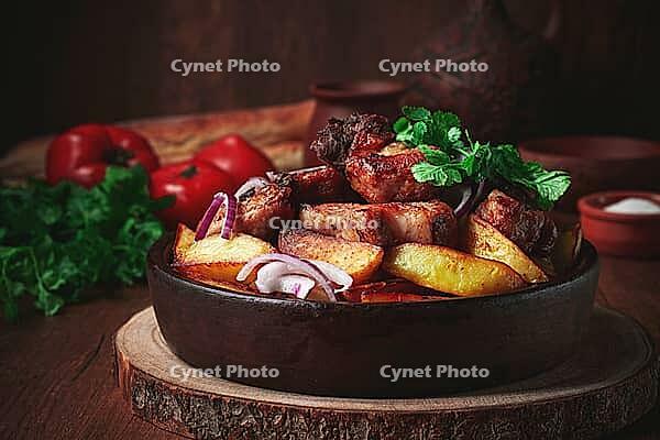 Ojakhuri, fried meat with potatoes, in ketsi, on a wooden table, Georgian cuisine, against a background of fresh ingredients [IBR125178020]