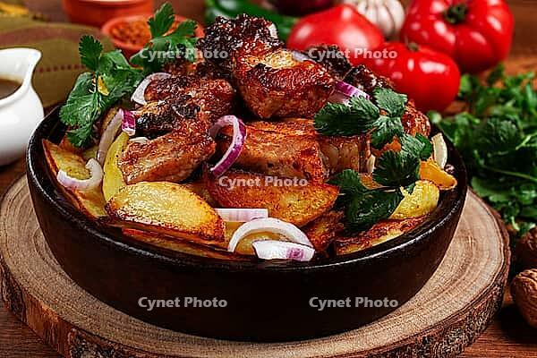 Ojakhuri, fried meat with potatoes, in ketsi, on a wooden table, Georgian cuisine, against a background of fresh ingredients [IBR125178021]