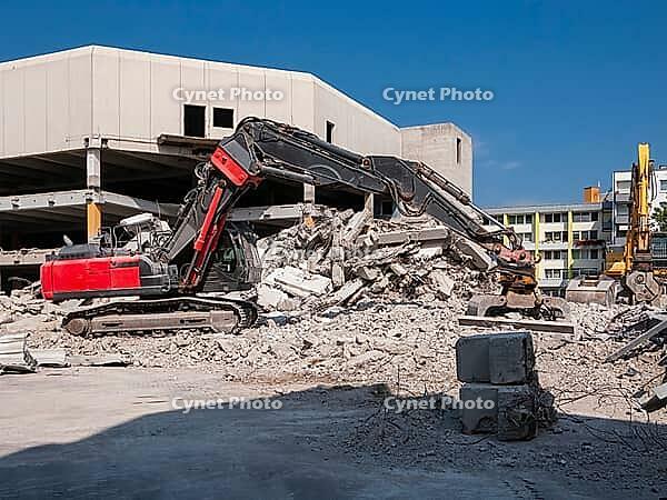 Red demolition excavator with grab in front of demolition building [IBR125180344]