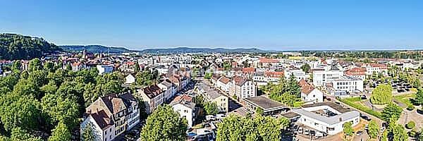 A wide-angle panorama from the air shows the city of Homburg on a sunny day. Residential buildings and trees are in the foreground, while the city center with streets and shops runs through the middle. In the background, wooded hills and the distinctive S [IBR125180379]