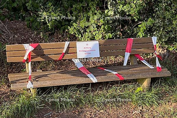Blocked park bench with warning sign and barrier tape in sunlight, Guxhagen, Hesse, Germany [IBR125180393]