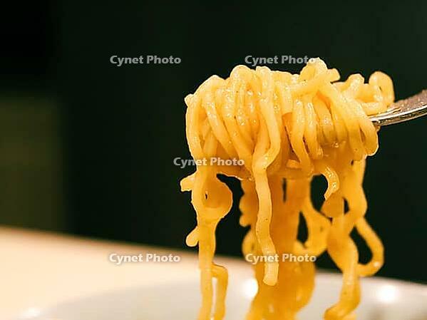 Close-up of ramen or noodles being lifted by a fork against a dark background [IBR125185843]