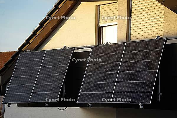 An attic apartment with a balcony and large solar panels. The evening sun is still shining with golden light on the windows and balcony door, but the solar panels are already in the shade [IBR125185849]