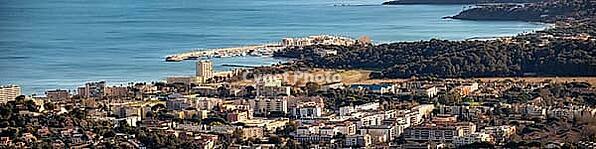 Broad view across the Bormes-les-Mimosas coastline with urban buildings, green hills and La Faviere marina under a clear sky, Bormes-les-Mimosas, La Faviere, Var, Provence-Alpes-Cote d Azur, France [IBR125185854]