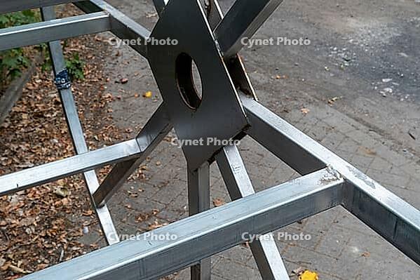 A metal frame is set up on the ground in a city street. It is being assembled with steel parts and tools around. There is a mix of dirt and leaves on the ground, Borken, NRW, Germany [IBR125185857]