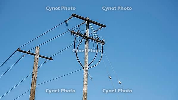 Low angle view of wooden utility poles with overhead power lines and equipment against a clear blue sky [IBR125185864]