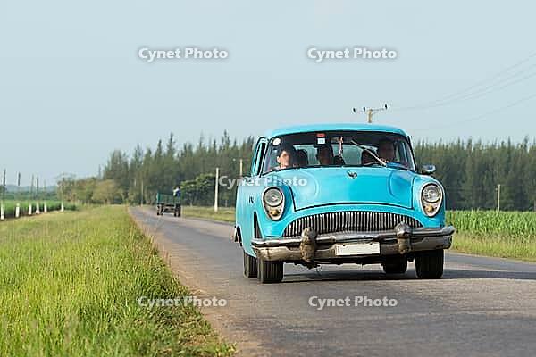 Blauer amerikanischer Oldtimer fährt auf der Landstrasse im Landesinneren von Kuba Blue American classic car traveling on the road in the countryside of Cuba [IBR125188218]