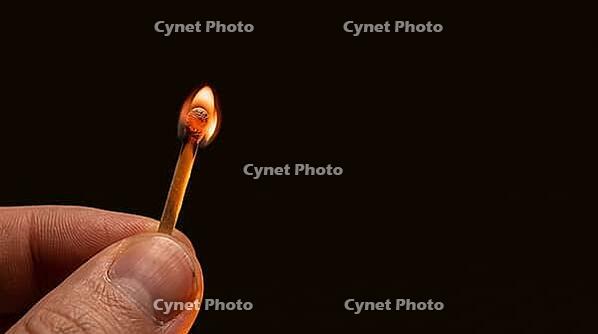 Single wooden matchstick in moment of ignition, tiny orange-white phosphorus flame just forming at tip, fingers lit from match-light below, Glimmers of Wonder winter hope and intimate festive light concept, dark background, studio shot, AI generated [IBR125200735]