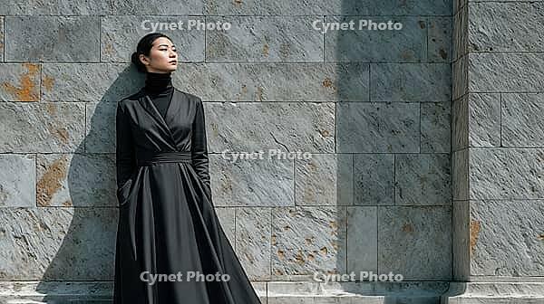 Asian fashion model in a black formald dress resting against a brick stone wall. Confident expression. Hands in pockets, AI generated [IBR125237530]