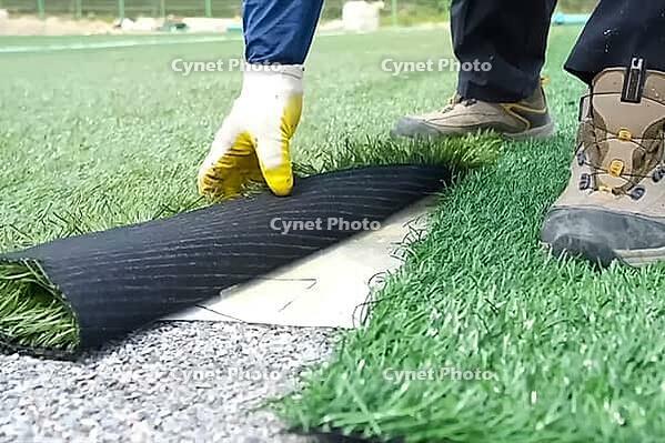 Spreading artificial turf in the stadium, rolling out rolls of lawn and leveling [IBR125242408]