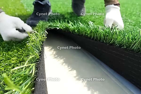 Spreading artificial turf in the stadium, rolling out rolls of lawn and leveling [IBR125242427]