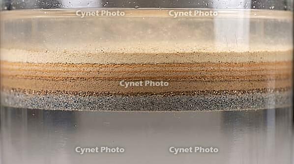 Abstract macro of particulate matter settling into distinct layered bands within a liquid suspension, laboratory sedimentation process, studio shot, AI generated [IBR125242478]