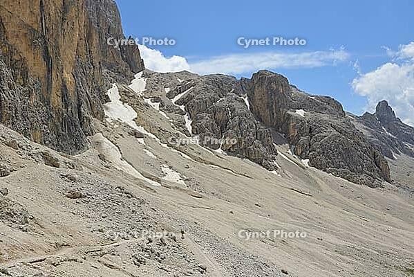 Hiking on a rocky mountain trail with boulders and peaks under a blue sky [IBR125261554]