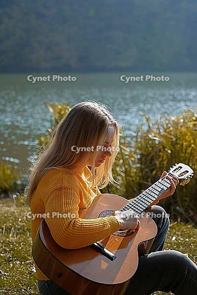 Blonde woman playing string guitar outdoors in autumn forest. Concept of sound therapy, mental health and wellness rituals. Calmness tranquility audio-sensory practices. Aura farming energy holistic health [IBR125261599]