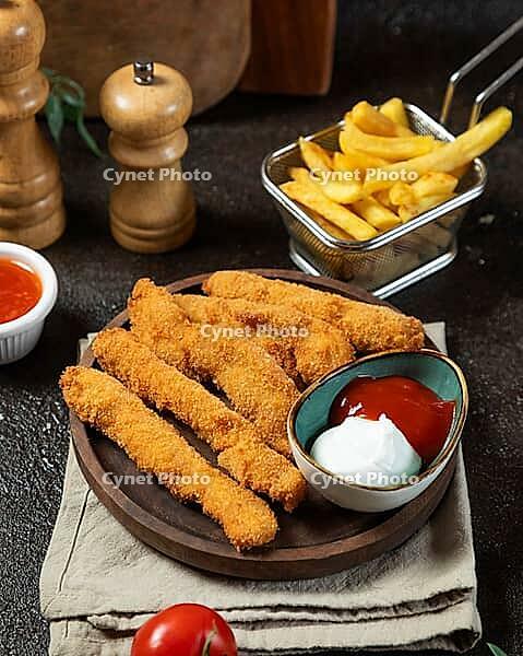 Crispy breaded chicken strips served on a wooden plate with french fries, ketchup, mayonnaise, and fresh tomatoes [IBR125261609]