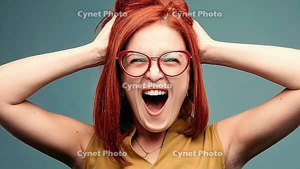 Front view of happy and positivity red haired woman in eyeglasses shouting holding head by hands, looking at camera. Emotionally girl smiling and surprised, having good shock. Drive and happy concept [IBR125261615]