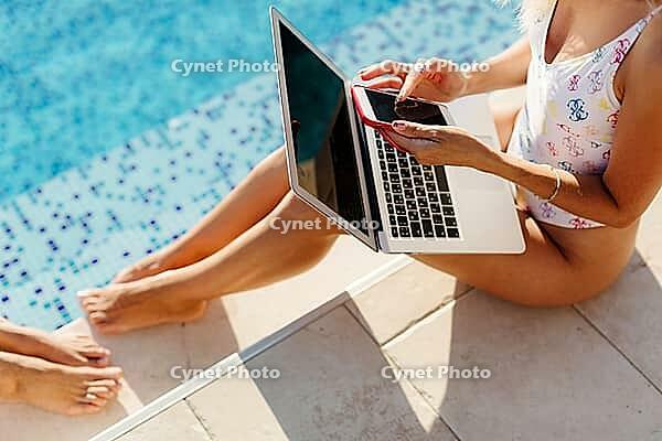 Woman using laptop and smartphone on beach pool. Woman freelancer working on laptop on edge of pool. Female study online easily. Using multiple devices [IBR125261627]