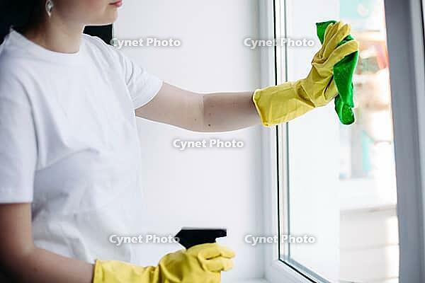 Crop of incognito brunette housewife cleaning dirty window. Housemaid wearing white t shirt and yellow protective gloves wiping glass with rag. Concept of housework and apartment service [IBR125261634]