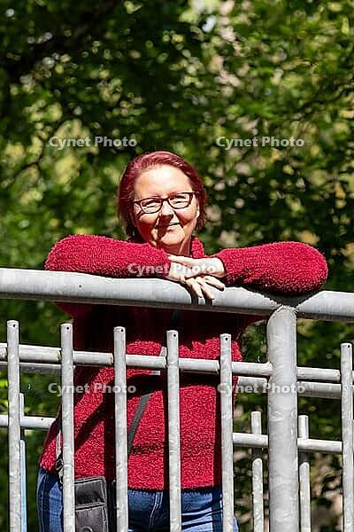 Woman with red hair and glasses wearing a red sweater leaning on a metal railing [IBR125261640]