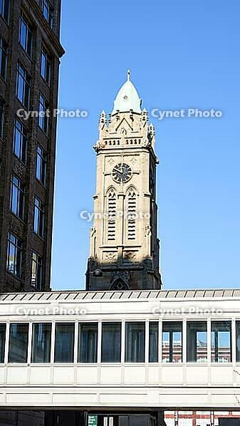 Low angle view of a historic clock tower framed by modern urban buildings against clear blue sky [IBR125280298]
