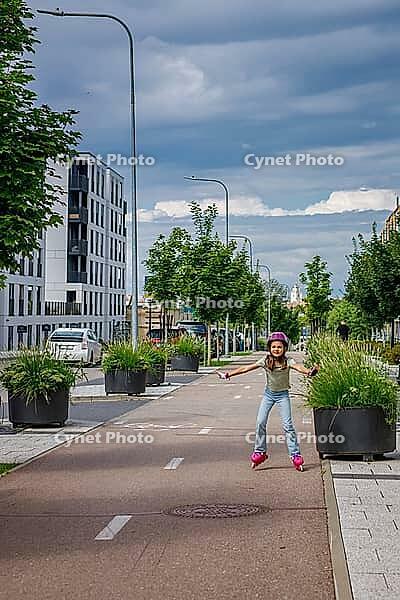 Child practicing inline skating on a designated metropolitan track surrounded by green trees and contemporary architecture representing outdoor fitness and summer sports [IBR125280376]