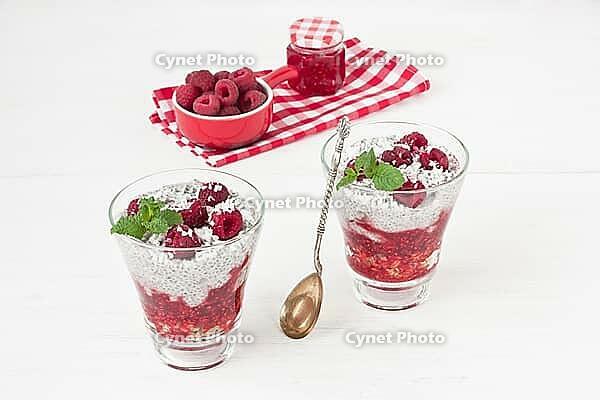 Chia seeds coconut milk pudding with oatmeal granola, raspberry jam, coconut chips and mint in glass on white wooden background [IBR125304594]