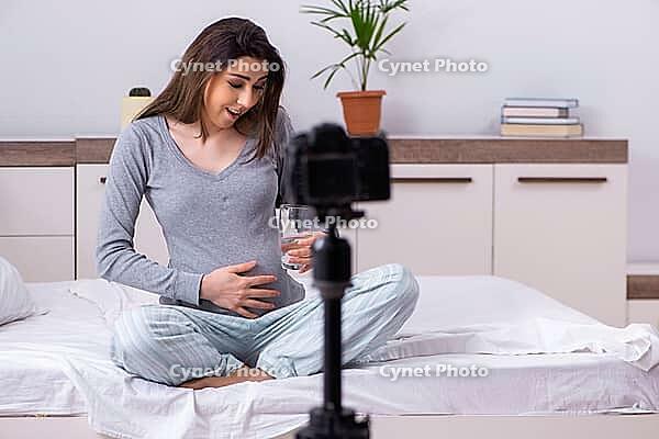 The pregnant woman is recording video for her blog [IBR125304626]