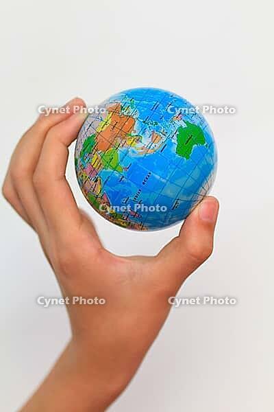 A child's hand holding up a small colored world globe on an isolated background [IBR125324098]