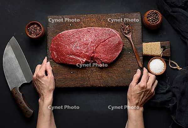 Raw beef tenderloin lies on a wooden cutting board and spices for cooking on a black table, top view and large kitchen knife [IBR125331122]