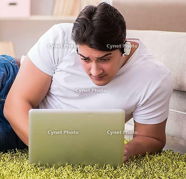 The man working on a laptop on the carpet at home [IBR125331123]