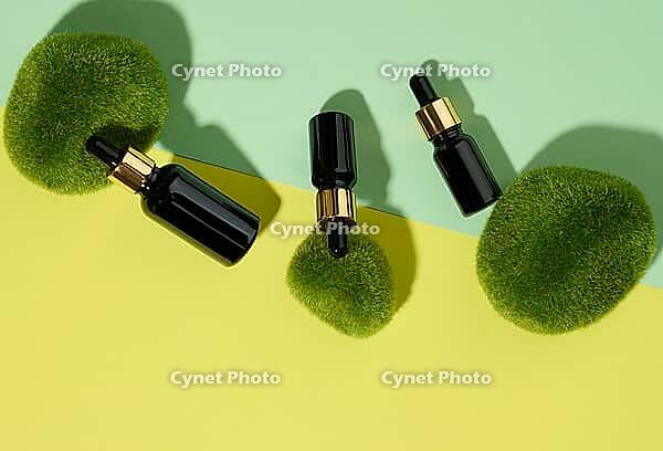 Glass cosmetic brown bottles with a pipette on a green-yellow background with pieces of moss. Cosmetics SPA branding mockup, top view [IBR125331127]