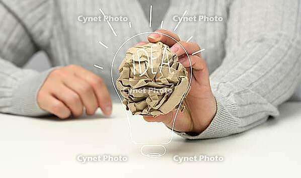Female hand holds a crumpled brown ball of paper. New idea, brainstorming [IBR125331137]