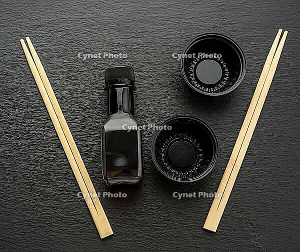 Wooden sticks for sushi, bottle of soy sauce and disposable plastic plates on black background, utensils for delivery [IBR125331142]