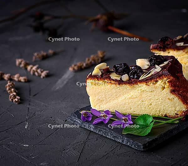 Piece of cheesecake poured with chocolate and almond shavings on a black background, empty space [IBR125331155]